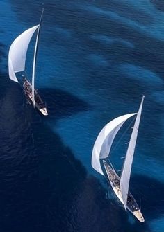 two sailboats sailing in the ocean with blue water and one boat has white sails