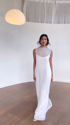 a woman in a white dress standing on a wooden floor next to a light fixture