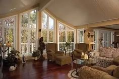 a living room filled with lots of furniture next to tall glass windows on top of a hard wood floor