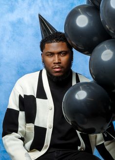 a man wearing a party hat sitting in front of balloons and posing for the camera