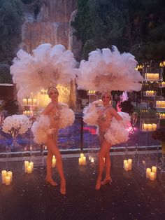 two women are dressed in white feather pom - poms and holding lit candles