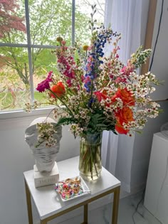 a vase filled with lots of colorful flowers on top of a table next to a window