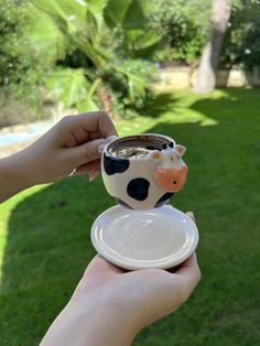 a person holding a small cup with a cow on it in their left hand and a saucer to the side