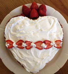 a heart shaped cake with white frosting and strawberries on the top is sitting on a plate