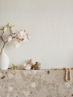 a vase with flowers and beads sitting on a shelf in front of a white wall