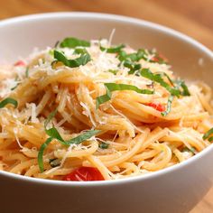 a white bowl filled with pasta and topped with parmesan cheese, tomatoes and basil