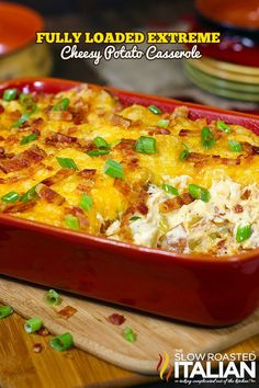 a red casserole dish with cheese and green onions in it on a wooden cutting board