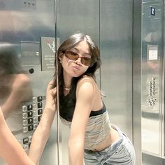 a woman leaning against a wall in front of a metal locker with buttons on it