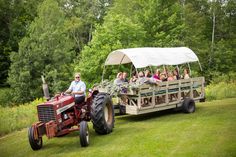 a tractor pulling a trailer with people in it on the grass near trees and bushes