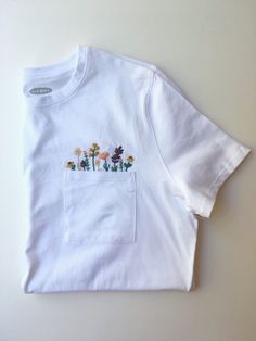 a white t - shirt with flowers embroidered on the front and pocket at the back