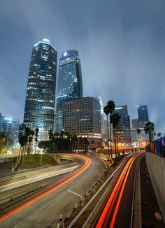 the city skyline is lit up at night with lights streaking down from tall buildings