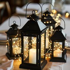 three lit lanterns sitting on top of a table covered in white linens and lights