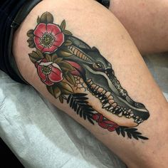 a woman's thigh with an alligator and flowers tattoo design on it, sitting on a bed