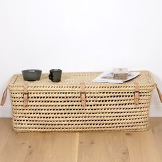 a wicker coffee table with two cups on it and a magazine in the basket