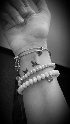 a woman's arm with three bracelets on it and two birds in the sky