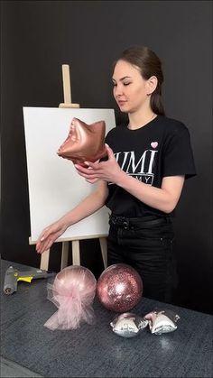 a woman in black shirt holding a brown shoe next to other ornaments and an easel