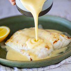 someone is pouring sauce on some fish in a green dish with lemon wedges next to it