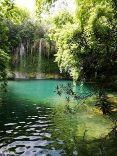 a body of water surrounded by lush green trees and waterfall in the middle of it