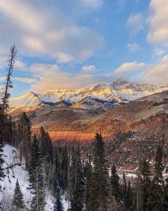 the mountains are covered with snow and trees in the foreground, under a cloudy blue sky