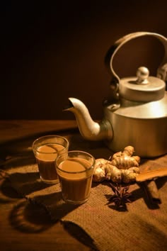 a tea pot and two glasses filled with liquid next to garlic on a tablecloth