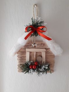 a wooden house ornament hanging on a wall with snow and red ribbon around it