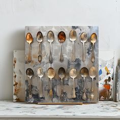 an assortment of spoons are displayed on a shelf in front of some paintbrushes