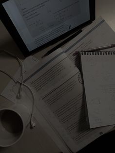 a computer monitor sitting on top of a desk next to papers and a cup filled with coffee