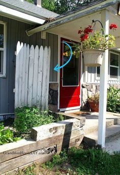 a red door sits in front of a white house with flowers growing on the porch