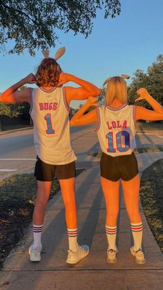 two girls in basketball uniforms are standing on the sidewalk with their hands behind their backs