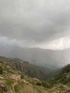 the mountains are covered with green grass and trees, while dark clouds hover over them