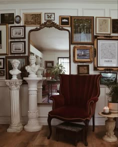 a red chair sitting in front of a mirror on top of a wall covered in pictures