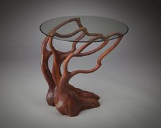 a wooden table with glass top and tree design on the base, sitting on a gray background