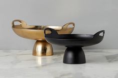 two black and gold bowls sitting on top of a marble counter next to each other