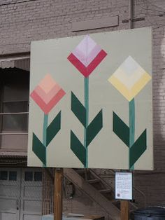 a large sign with flowers painted on it in front of a brick building and stairs