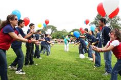 a group of people standing on top of a lush green field holding onto red, white and blue balloons