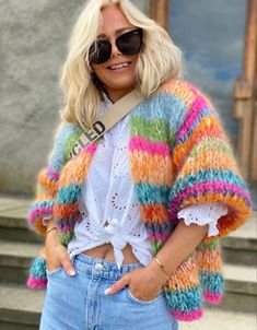 a woman with blonde hair wearing sunglasses and a multicolored cardigan sweater standing on steps