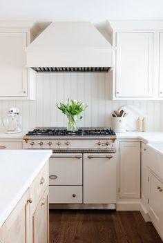 a kitchen with white cabinets and wooden floors has a vase filled with flowers on the stove