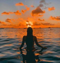 a woman is sitting in the water at sunset