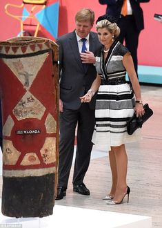 two people standing next to each other in front of a large wooden pole with designs on it