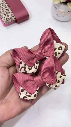 a hand holding a pink and white bow on top of a piece of fabric with leopard print