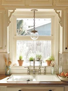 a kitchen sink sitting under a window next to a potted plant in a vase