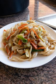 a white plate topped with noodles and veggies on top of a marble counter