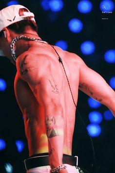 a shirtless man with tattoos on his chest and hands behind his back, standing in front of blue lights