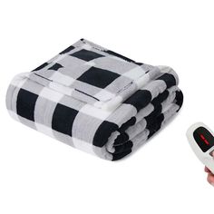 a hand holding a remote control next to a stack of black and white plaid blankets