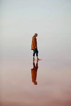 a person walking on the beach with their reflection in the water and sky behind them