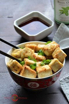 a bowl filled with tofu and green onions next to dipping sauce on a table