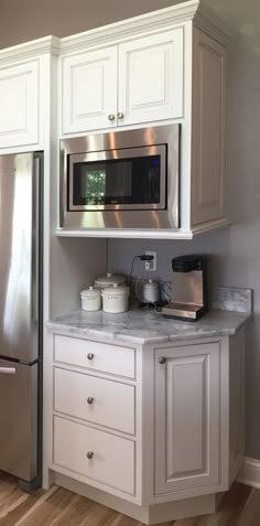 a kitchen with white cabinets and stainless steel microwave above the countertop, in front of a window