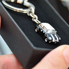 a hand holding a key chain with a car charm on it's end in a black box