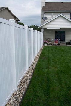 a white fence in front of a house with grass and rocks on the side walk