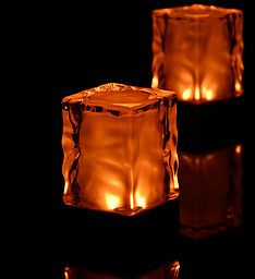 two lit candles sitting next to each other in front of a black background with reflections on the floor